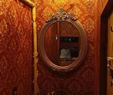 Small ornate washroom with chandelier, round carved mirror, patterned red wallpaper and wooden basin at Ryokan La Luna, Shizuoka
