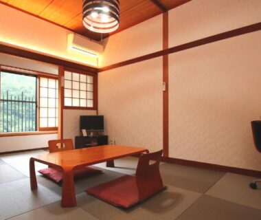 Tatami room with low table, floor chairs, shoji window and desk at Ryokan Maruya in Ōita, Kyūshū
