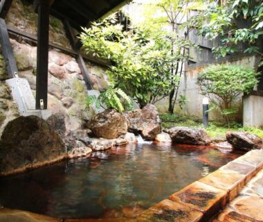 Stone outdoor onsen bath with rock edging and lanterns at Ryokan Maruya in Oita, Kyushu