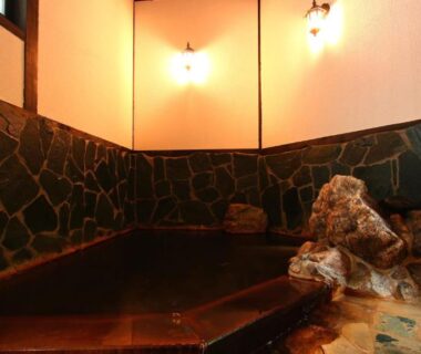 Indoor stone onsen bath with rock feature at Ryokan Maruya in Ōita, Kyūshū, Japan