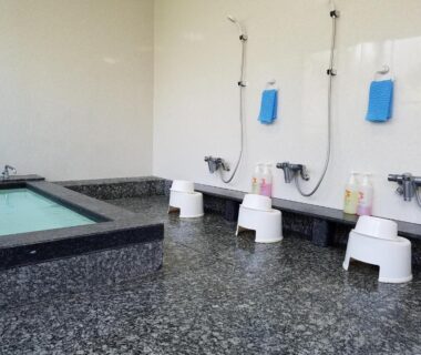 Communal indoor bathing area with stone soaking tub, shower stools and toiletries at Ryokan Matsukaze, Nagano