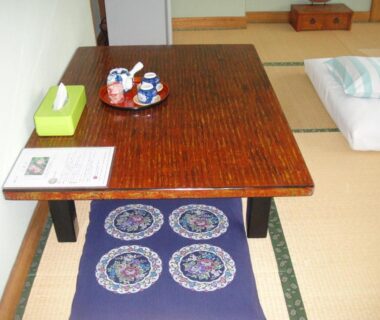 Tatami flooring with low wooden table, floor cushions and folded futon in a Ryokan Matsukaze room, Nagano