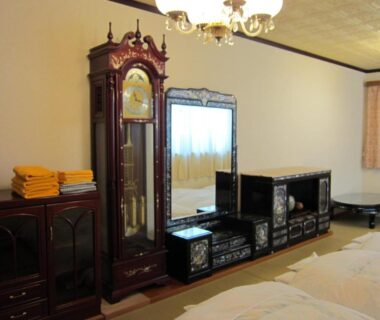 Guest room with twin beds, large grandfather clock, dresser and stacked towels at Ryokan Matsukaze in Nagano