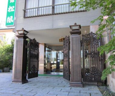 Decorative iron entrance gates opening to Ryokan Matsukaze lobby with stone paving and glass doors in Nagano