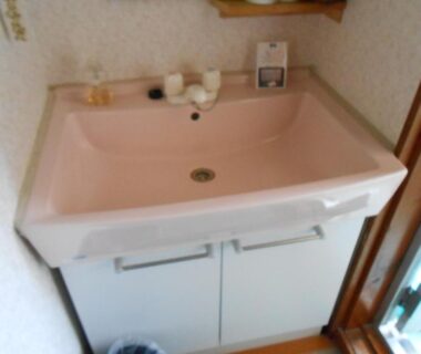 Pink ceramic basin with under-sink cabinet, faucet and toiletries in compact ryokan wash area, Kanagawa Japan