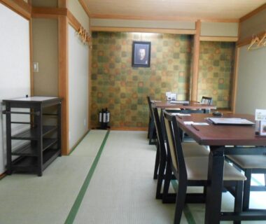 Tatami dining room with low table and chairs, sliding screens and patterned wall at Ryokan Matsushima, Kanagawa