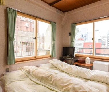 Tatami room with futons, green curtains, TV and city view at Ryokan Mikawaya, Tokyo