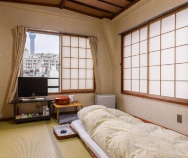 Tatami room with futon, shoji screens, low table and city view at Ryokan Mikawaya Tokyo