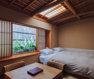 Tatami room with low wooden table, twin beds, shoji screens and plant-lined window at Ryokan Motonago Kyoto