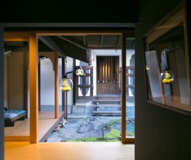 View through corridor to stone courtyard with hanging lanterns and sliding doors at Ryokan Mugen Kyoto