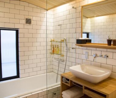 Tiled bath with bathtub, vessel sink, wooden vanity and frosted window at Ryokan Mugen, Kyoto