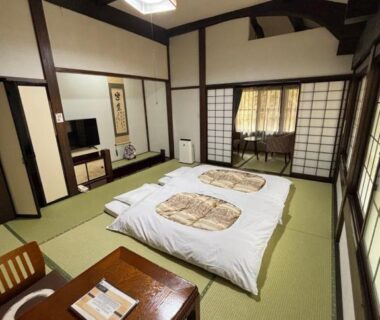 Traditional tatami room with futon bedding, shoji screens, low wooden table and exposed beams at Ryokan Murayama in Gifu