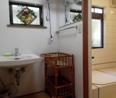 Compact washroom with sink, mirror, wicker shelves and tiled bathing area in Ryokan Nakajimaya, Kyoto
