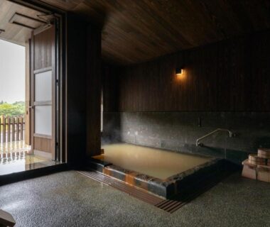 Indoor stone soaking bath with wooden walls, open door to balcony and bathing buckets at Ryokan Nanjoen in Kumamoto