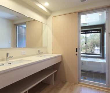 Double sink vanity and mirror leading to bathing area with soaking tub and garden view at Ryokan Nenrinbo Kyoto