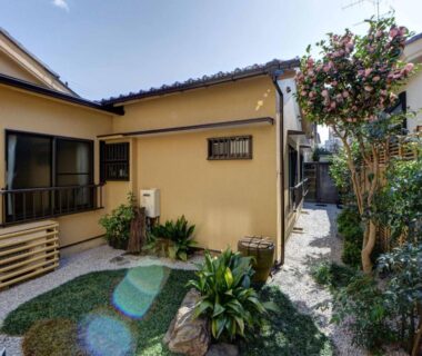 Sunny courtyard with gravel path, small planted garden and traditional single-story ryokan exterior at Ryokan Niko in Tokyo