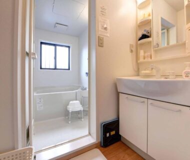 Compact washroom with vanity, mirror and tiled bathing area with stool at Ryokan Niko, Tokyo