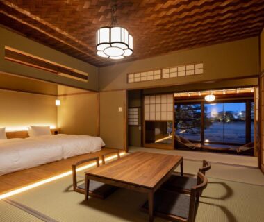 Tatami room with low beds, wooden table, shoji screens and exterior view at Ryokan Onomichi Nishiyama, Hiroshima