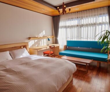 Double bed and turquoise sofa on wooden floor with large window at Ryokan Plum, Kanagawa, Kantō, Japan