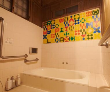 Indoor bathtub with white tile, colorful geometric accent tiles, grab bars and toiletries in ryokan bathroom