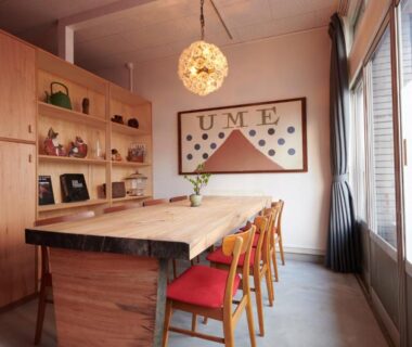 Long wooden communal table with mixed chairs, pendant light, shelving and framed UME art at Ryokan Plum, Kanagawa