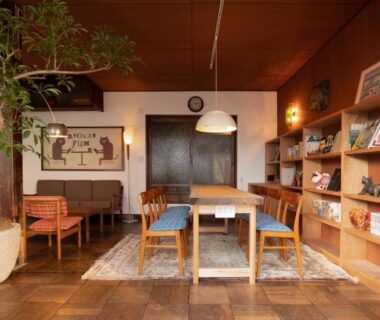 Wood-floored lounge with long table, bookshelves and seating at Ryokan Plum in Kanagawa, Kantō