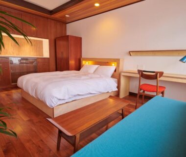 Room with wooden platform bed, desk, teal sofa, shoji screen and warm lighting at Ryokan Plum in Kanagawa