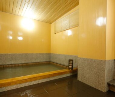 Small indoor onsen with wooden walls, stone base and warm lighting at Ryokan Sanga in Kyoto