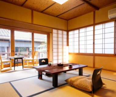 Spacious tatami room with low wooden table, zabuton seating and shoji screens opening to a wooden veranda at Ryokan Sanga