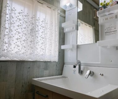 Compact washbasin with mirror, shelving, and floral lace curtain in ryokan bathroom with soft natural light