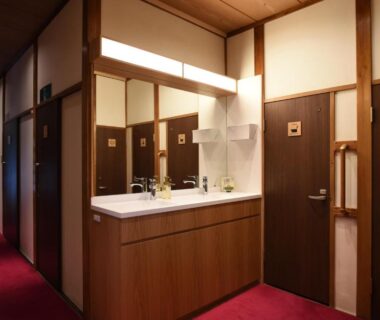 Hallway with double washbasins, wooden doors, shoji panels and red carpet at Ryokan Sansuiso, Tokyo