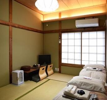 Tatami room with futons, shoji screens, low table and TV at Ryokan Sansuiso in Tokyo