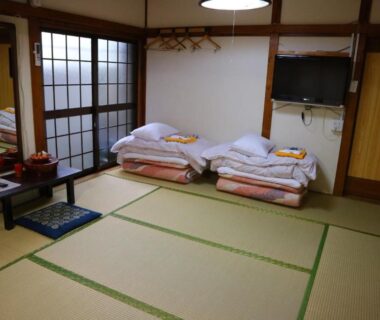 Traditional tatami room with folded futon bedding, shoji screens, low table and TV at Ryokan Sansuiso in Tokyo