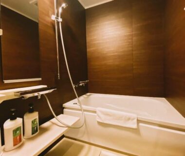 Compact modern bathroom with bathtub, hand shower, wood-tone wall panels and toiletries at Ryokan Sawaya Honten, Kyoto