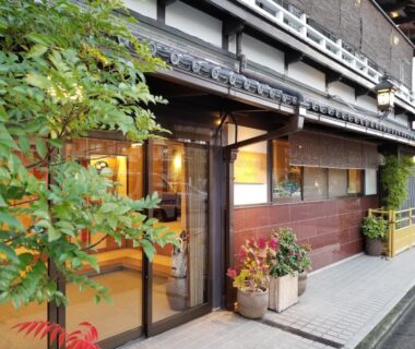 Wooden ryokan entrance with glass doors, potted plants and bamboo blinds at Ryokan Sawaya Honten Kyoto