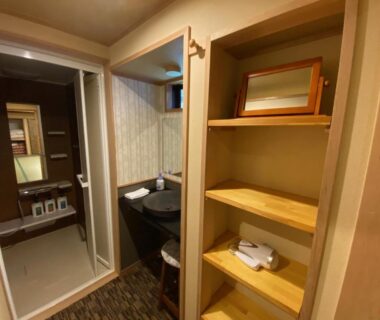 Wooden shelving beside a compact wash basin and doorway leading to a bathroom in Ryokan Sawaya Honten Kyoto