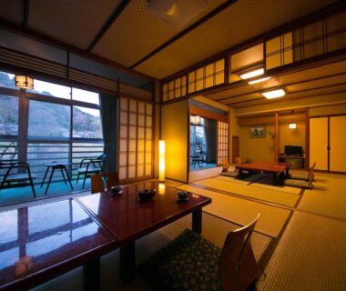 Spacious tatami room with low table, shoji screens and balcony overlooking water and distant hills at Ryokan Seishounagon Mie
