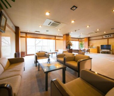 Spacious ryokan lounge with sofas, glass-topped tables and large windows overlooking outdoor greenery in Mie