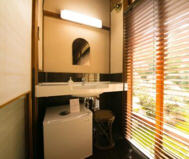 Bright washbasin with mirror, compact washer and wooden blinds overlooking greenery at Ryokan Sennari Oita