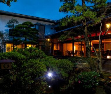 Lantern-lit garden courtyard with trees and traditional wooden exterior at Ryokan Sennari in Ōita, Kyūshū