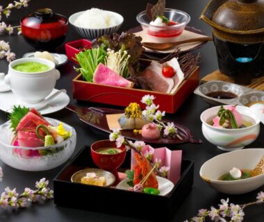 Lacquered trays with sashimi, simmered vegetables, pickles and small ceramic bowls with floral garnish