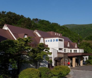 White ryokan building with pitched roofs and surrounding forested hills in Fukushima