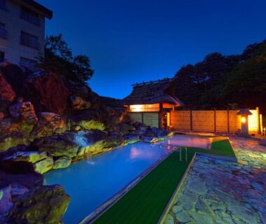 Nightlit open-air onsen with rock pool and traditional wooden bathhouse at Ryokan Tamagoyu, Fukushima, Tōhoku