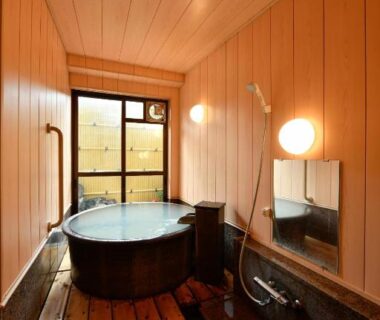 Round wooden soaking tub with wash area and window in Ryokan Tamura, Gunma