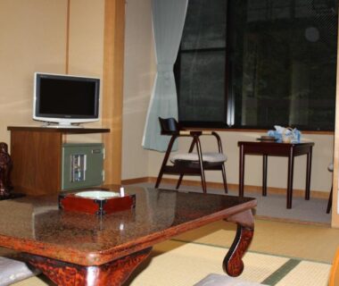 Traditional tatami room with low lacquered table, shoji screens, small television and window seating at Ryokan Tanaka, Gifu