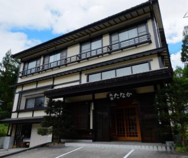 Three-story ryokan exterior with entrance, parking area and forested hillside in Gifu