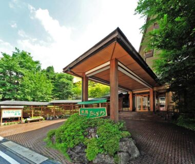 Covered wooden entrance and sign at Ryokan Tanigawa, paved driveway surrounded by trees in Gunma, Kantō