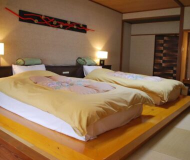 Two beds on raised wooden platform in tatami room with shoji and warm lamps at Ryokan Tanigawa, Gunma