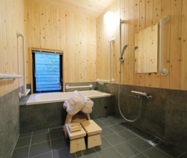 Wood-paneled bathing room with tiled floor, small soaking tub, shower and wooden stools at Ryokan Tanoya, Kyoto