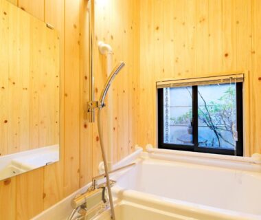 Indoor bath with tub, handheld shower, wood-paneled walls and small window with garden view at Ryokan Tanoya, Kyoto